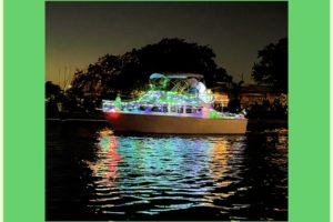 A boat, all decked out in Christmas lights cruises down a Florida canal after dark, showing off it’s colors.