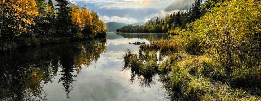 The morning sun rises above the water between two mountains.