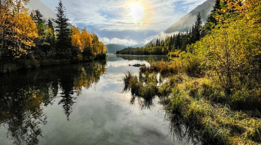The morning sun rises above the water between two mountains.