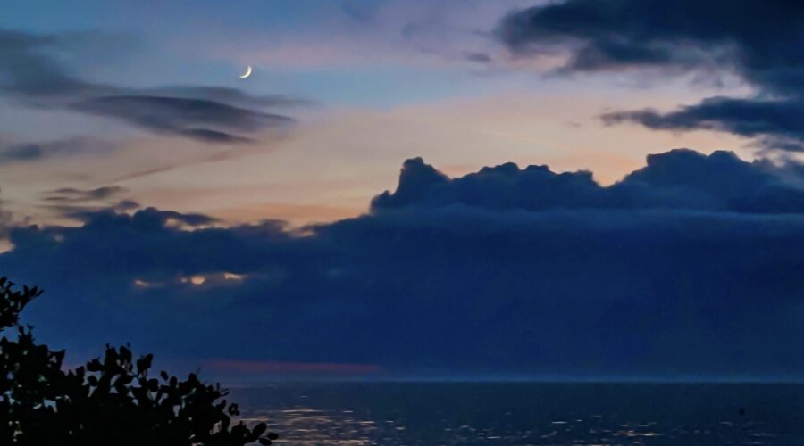After the sun has set, the sky continues to show some color as the moon appears.