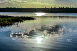 The bright, late afternoon sun causes reflections and a slight rainbow effect on a large lake.