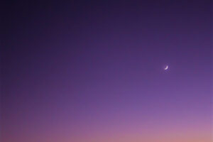 Venus rises above the quarter moon as the sun sets on a clear evening.