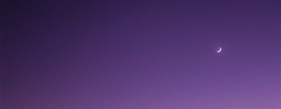 Venus rises above the quarter moon as the sun sets on a clear evening.