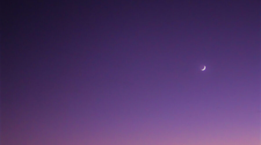 Venus rises above the quarter moon as the sun sets on a clear evening.